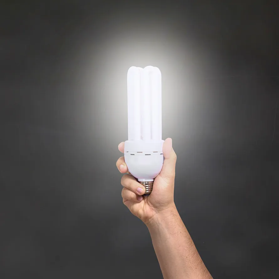 Eine Energiesparlampe in der Hand vor schwarzem Hintergrund